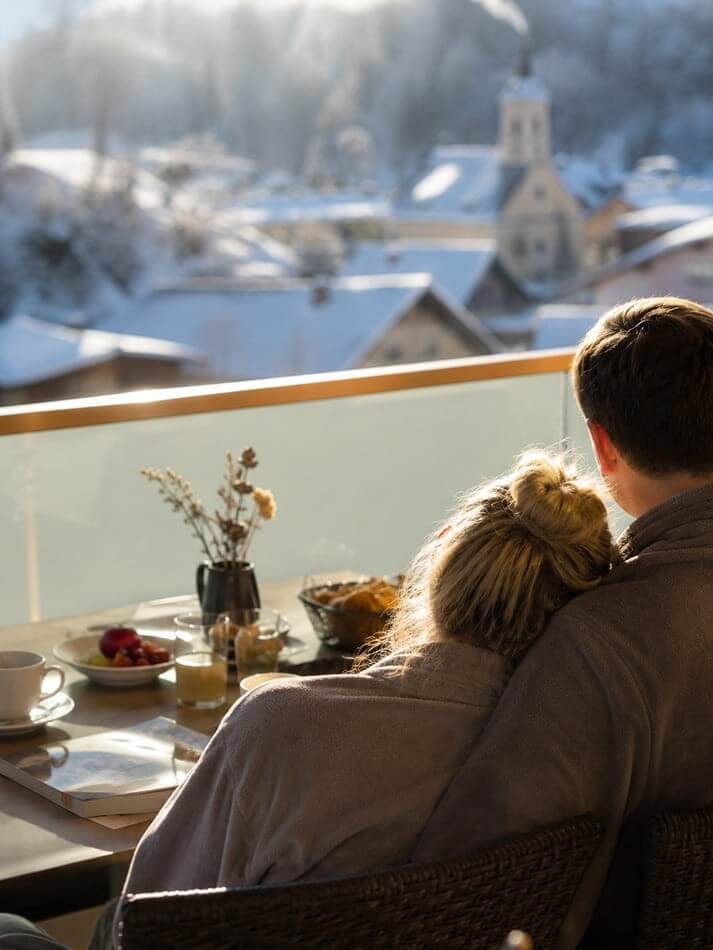 Paar genießt entspannte Wohlfühlmomente beim Frühstück auf dem Balkon mit Blick auf das winterliche Wagrain